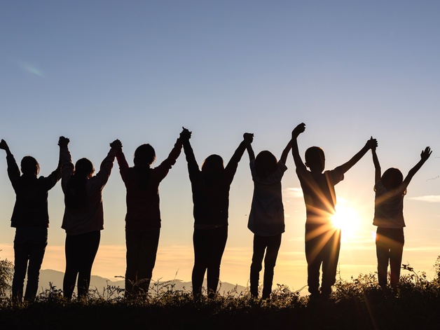 Silhouette of seven people holding hands with the sun rising behind them.