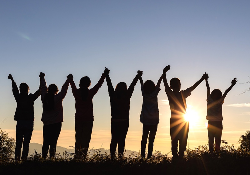 Silhouette of seven people holding hands with the sun rising behind them.